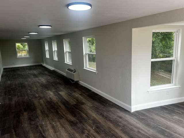 empty room featuring dark wood-type flooring, a wall mounted air conditioner, and plenty of natural light