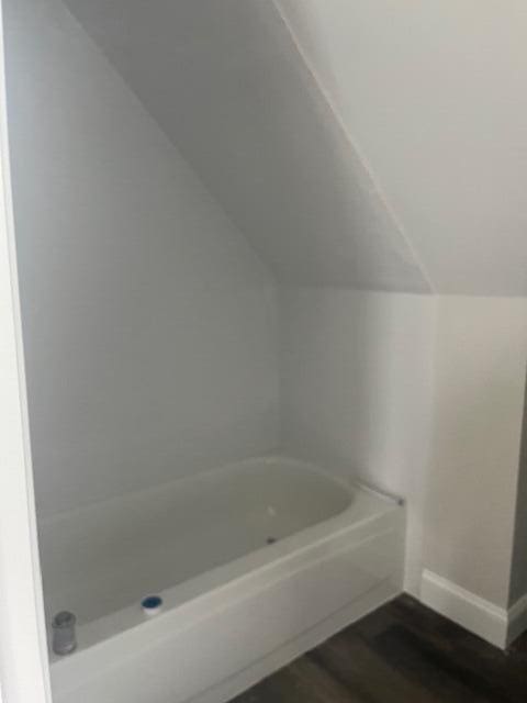 bathroom with vaulted ceiling, hardwood / wood-style flooring, and a bath