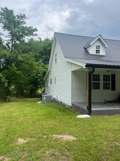 view of side of home featuring central air condition unit, a patio area, and a lawn