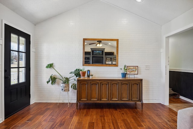 entryway with lofted ceiling, brick wall, ceiling fan, and dark hardwood / wood-style flooring