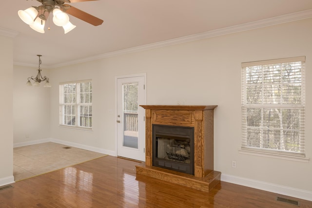 unfurnished living room featuring ornamental molding, ceiling fan with notable chandelier, and hardwood / wood-style flooring