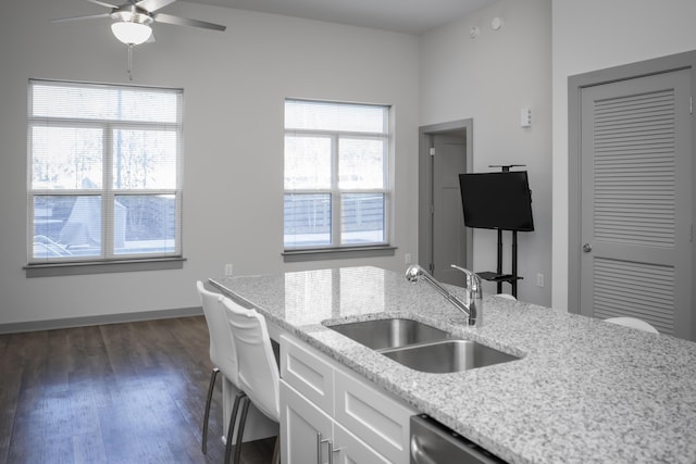 kitchen with white cabinets, a wealth of natural light, light stone countertops, and sink