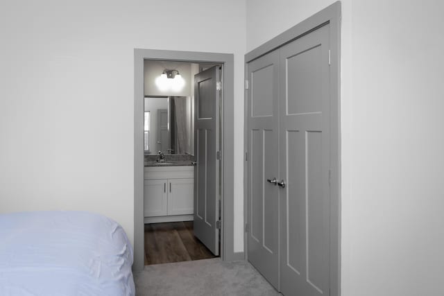 unfurnished bedroom featuring a closet, ensuite bathroom, sink, and dark carpet