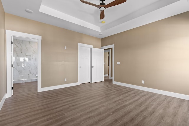 unfurnished bedroom featuring a tray ceiling, dark wood-type flooring, and baseboards