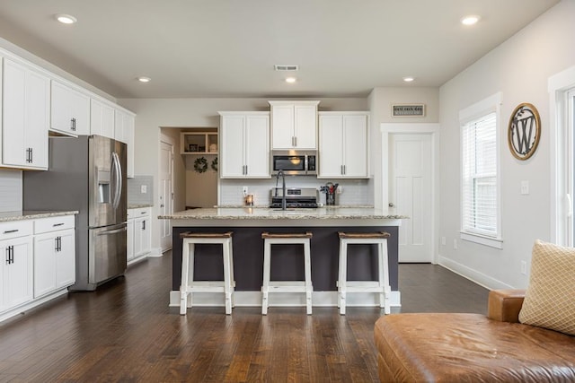 kitchen with white cabinetry, stainless steel appliances, tasteful backsplash, a kitchen island with sink, and light stone countertops