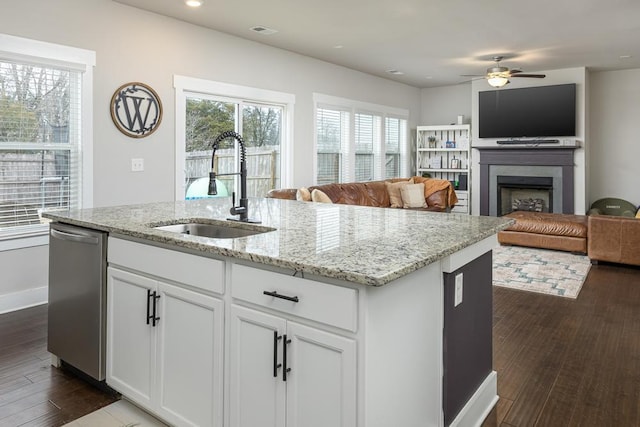 kitchen featuring a center island with sink, stainless steel dishwasher, sink, light stone countertops, and white cabinets