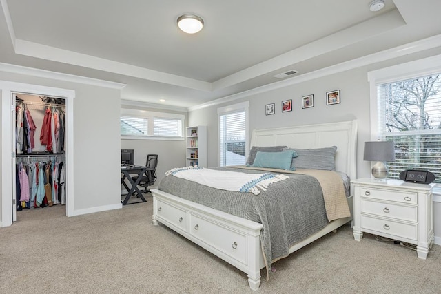 carpeted bedroom featuring a closet, a walk in closet, crown molding, and a raised ceiling