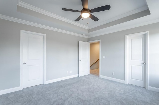 unfurnished bedroom with a raised ceiling, ceiling fan, crown molding, and light carpet