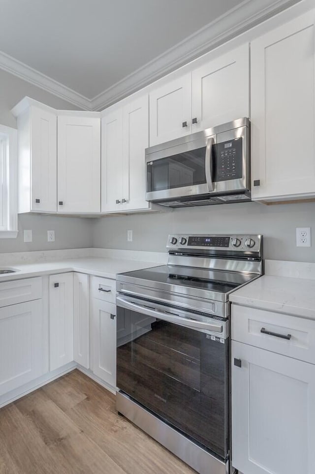 kitchen with light stone counters, stainless steel appliances, light hardwood / wood-style floors, crown molding, and white cabinets