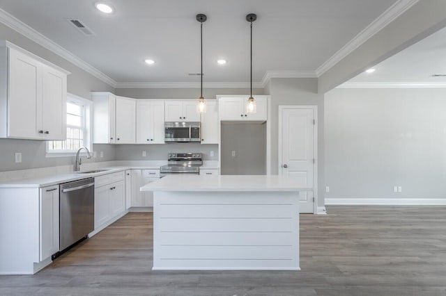 kitchen featuring hanging light fixtures, a kitchen island, white cabinets, appliances with stainless steel finishes, and sink