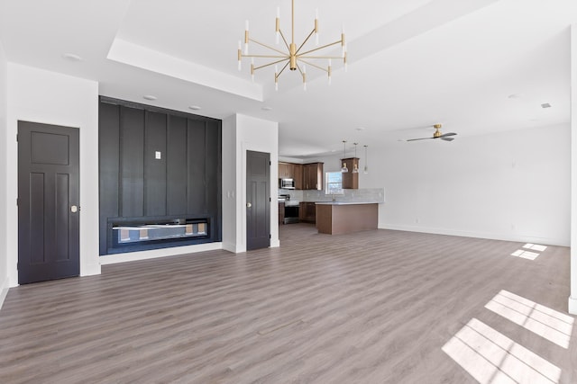 unfurnished living room featuring a sink, light wood-style flooring, baseboards, and ceiling fan with notable chandelier