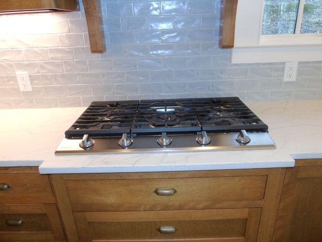 details with stainless steel gas cooktop, brown cabinetry, and decorative backsplash