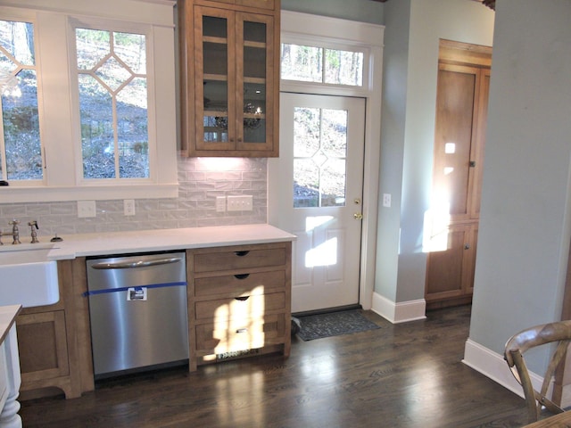 kitchen featuring light countertops, stainless steel dishwasher, brown cabinets, tasteful backsplash, and glass insert cabinets