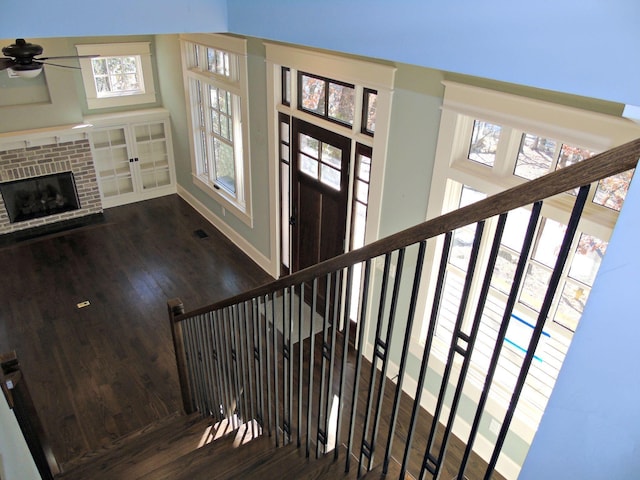 staircase featuring ceiling fan, a fireplace, wood finished floors, visible vents, and baseboards