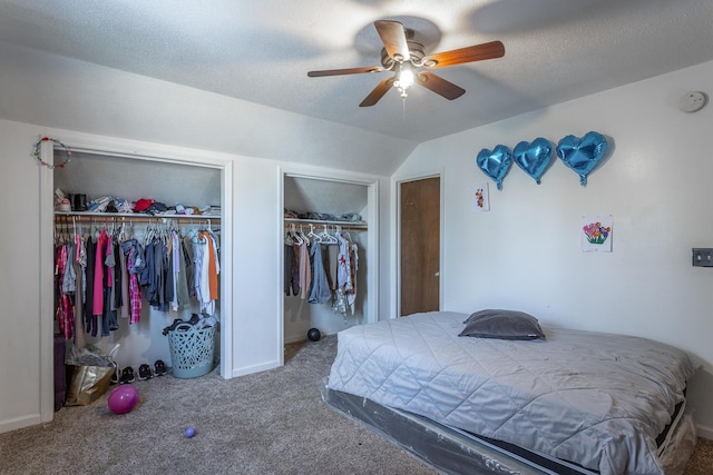 carpeted bedroom with vaulted ceiling, ceiling fan, two closets, and a textured ceiling