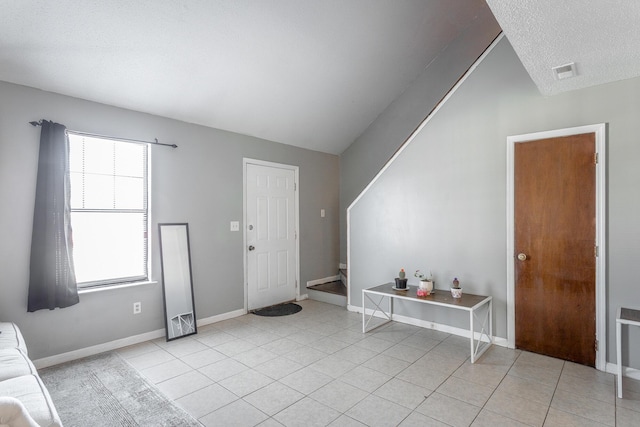 entrance foyer with a textured ceiling, light tile patterned flooring, and lofted ceiling