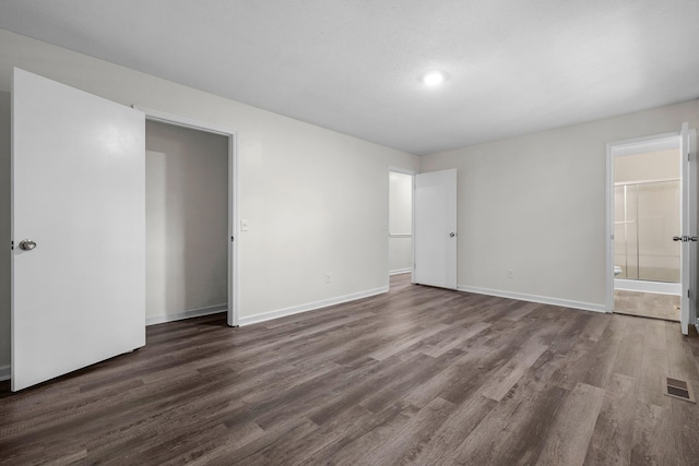 unfurnished bedroom with ensuite bathroom and dark hardwood / wood-style floors