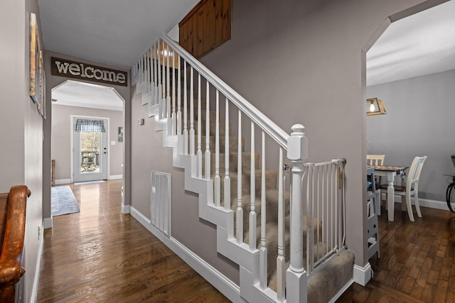 stairway with arched walkways, wood finished floors, and baseboards