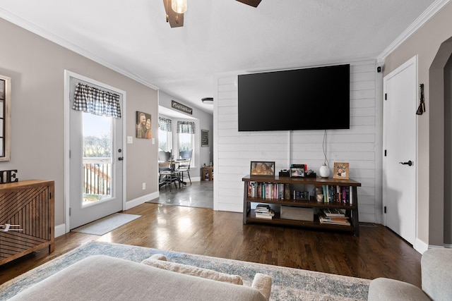 living area with crown molding, wood finished floors, baseboards, and ceiling fan