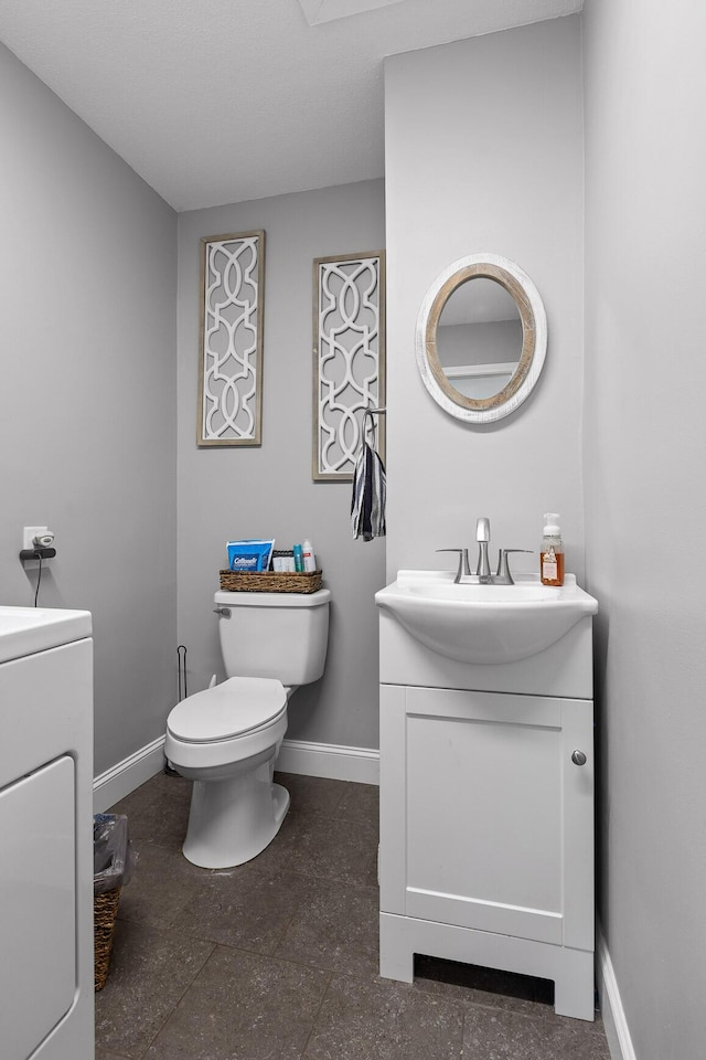 half bathroom with baseboards, vanity, washer / clothes dryer, and toilet