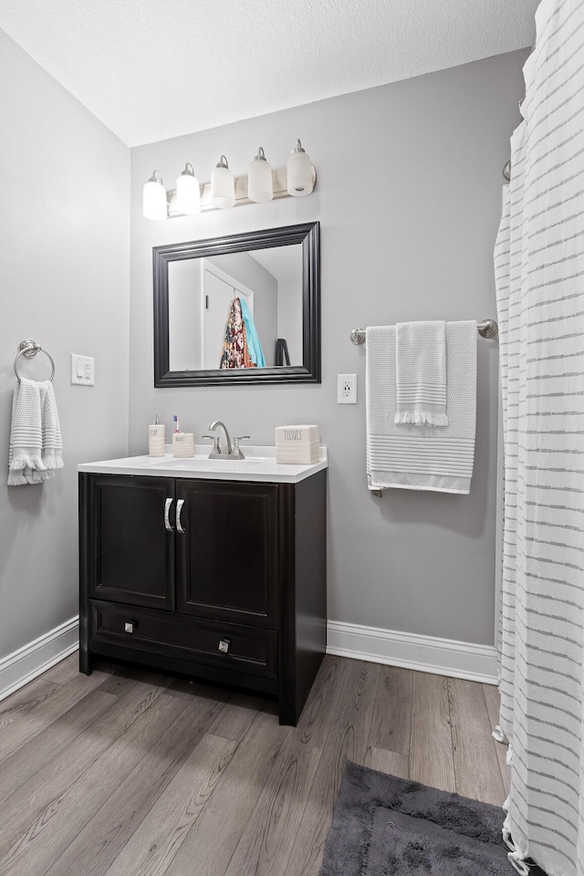 full bath with baseboards, wood finished floors, and vanity