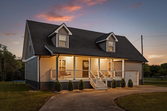 cape cod house featuring a trampoline, a porch, driveway, a front yard, and a garage