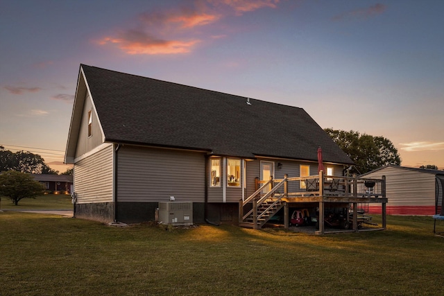 back of property at dusk featuring cooling unit, a wooden deck, a yard, stairs, and roof with shingles