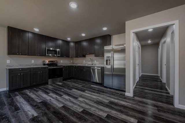 kitchen featuring baseboards, recessed lighting, a sink, stainless steel appliances, and dark wood-type flooring