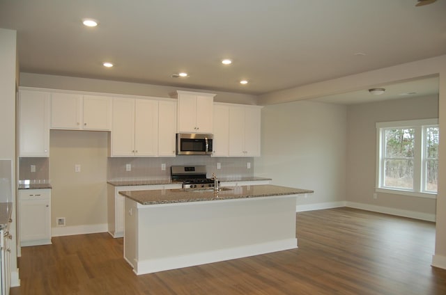 kitchen with stainless steel appliances, white cabinets, stone counters, tasteful backsplash, and a kitchen island with sink