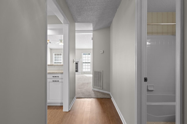 hallway featuring baseboards, light wood-style flooring, visible vents, and a textured ceiling