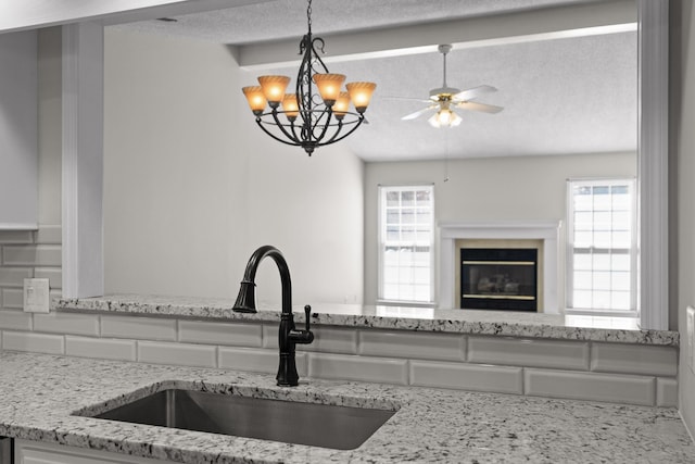 kitchen featuring a textured ceiling, light stone counters, a sink, a glass covered fireplace, and pendant lighting