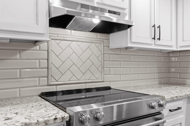 kitchen with light stone counters, backsplash, white cabinetry, stainless steel range with electric stovetop, and under cabinet range hood