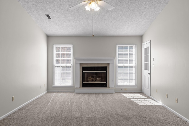 unfurnished living room with baseboards, a textured ceiling, a glass covered fireplace, and light colored carpet