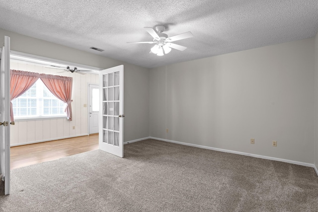 empty room featuring a textured ceiling, carpet floors, visible vents, a ceiling fan, and french doors