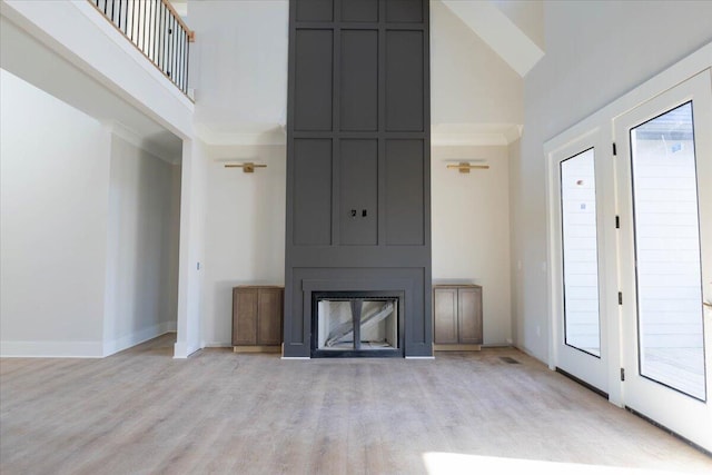 unfurnished living room featuring crown molding, a towering ceiling, a fireplace, and light hardwood / wood-style floors