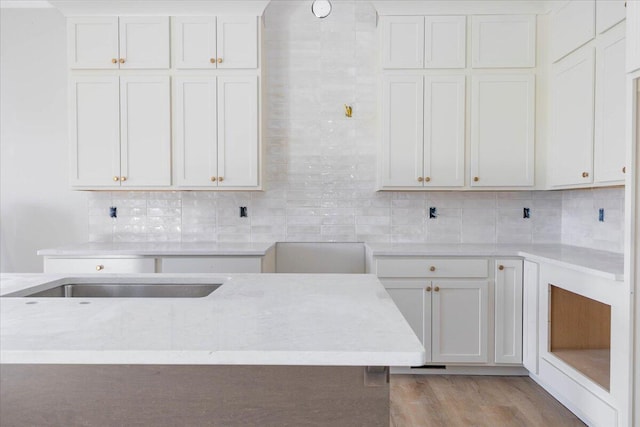 kitchen with white cabinetry, backsplash, light hardwood / wood-style floors, and light stone countertops