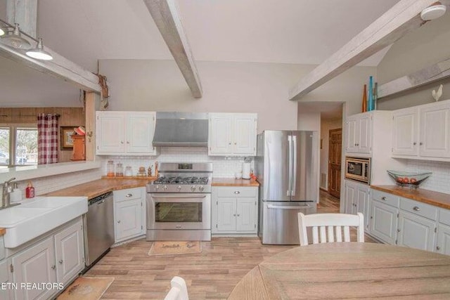 kitchen with white cabinetry, wall chimney range hood, stainless steel appliances, sink, and beam ceiling