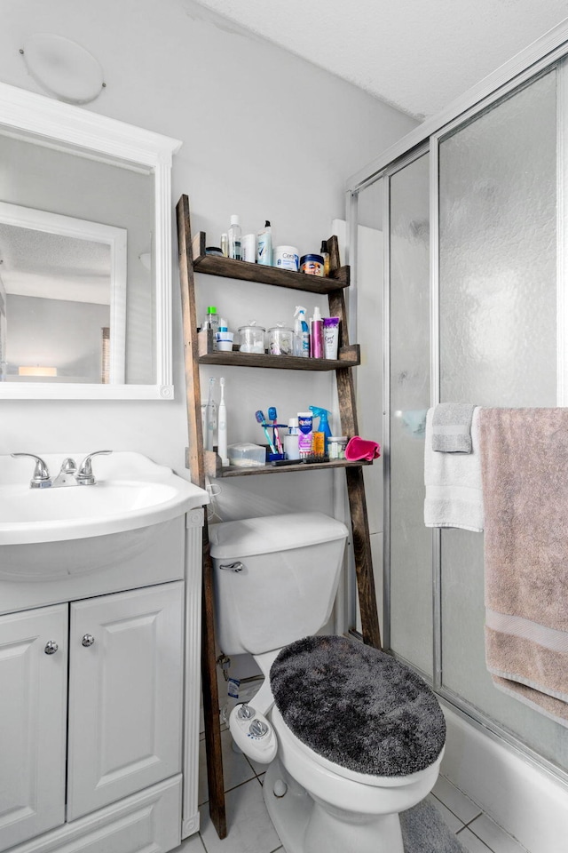 bathroom featuring a shower with door, vanity, tile patterned flooring, and toilet