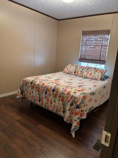 bedroom featuring dark hardwood / wood-style flooring, a textured ceiling, and ornamental molding