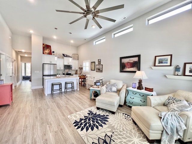 living room featuring ceiling fan, light hardwood / wood-style flooring, and a towering ceiling