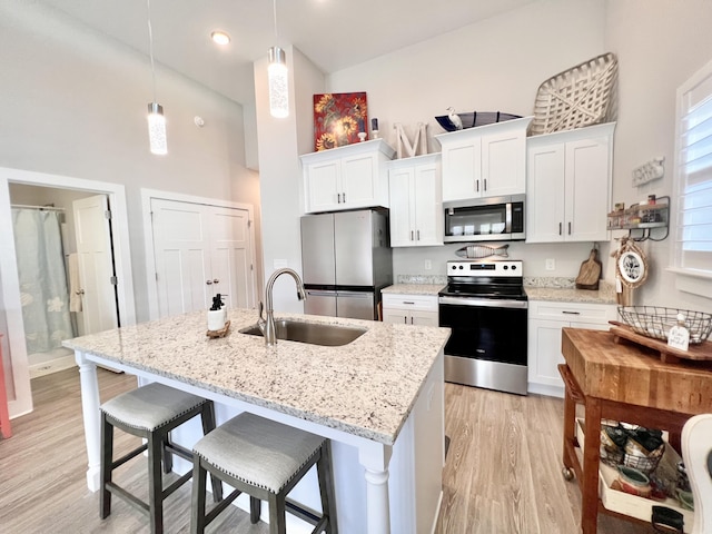 kitchen featuring sink, white cabinetry, hanging light fixtures, a kitchen island with sink, and appliances with stainless steel finishes