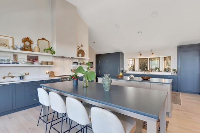 kitchen with blue cabinets, a kitchen bar, a center island, vaulted ceiling, and light hardwood / wood-style floors