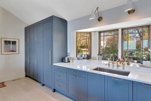 kitchen with sink, vaulted ceiling, blue cabinetry, and light wood-type flooring