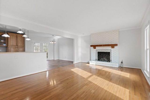 unfurnished living room featuring light wood-type flooring, crown molding, a fireplace, and a notable chandelier