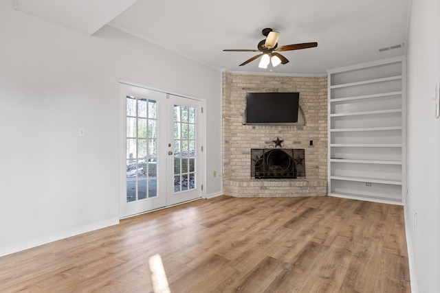 unfurnished living room featuring a brick fireplace, ceiling fan, light wood-type flooring, french doors, and ornamental molding