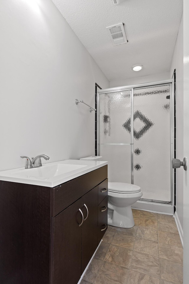 bathroom featuring a shower with shower door, vanity, toilet, and a textured ceiling