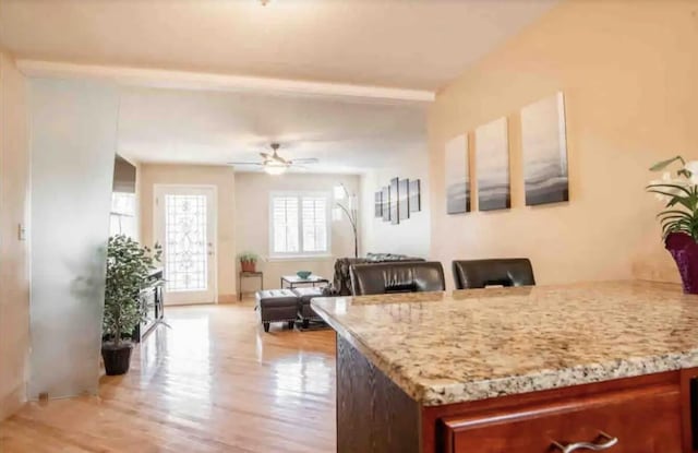 kitchen with ceiling fan, light stone counters, light hardwood / wood-style flooring, and beamed ceiling