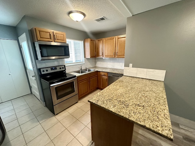 kitchen featuring appliances with stainless steel finishes, sink, kitchen peninsula, and light stone countertops