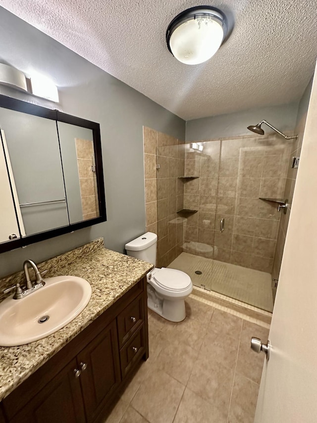 bathroom with toilet, vanity, tiled shower, and a textured ceiling