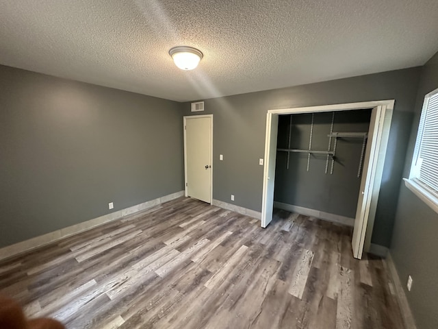 unfurnished bedroom with a textured ceiling, a closet, and hardwood / wood-style flooring